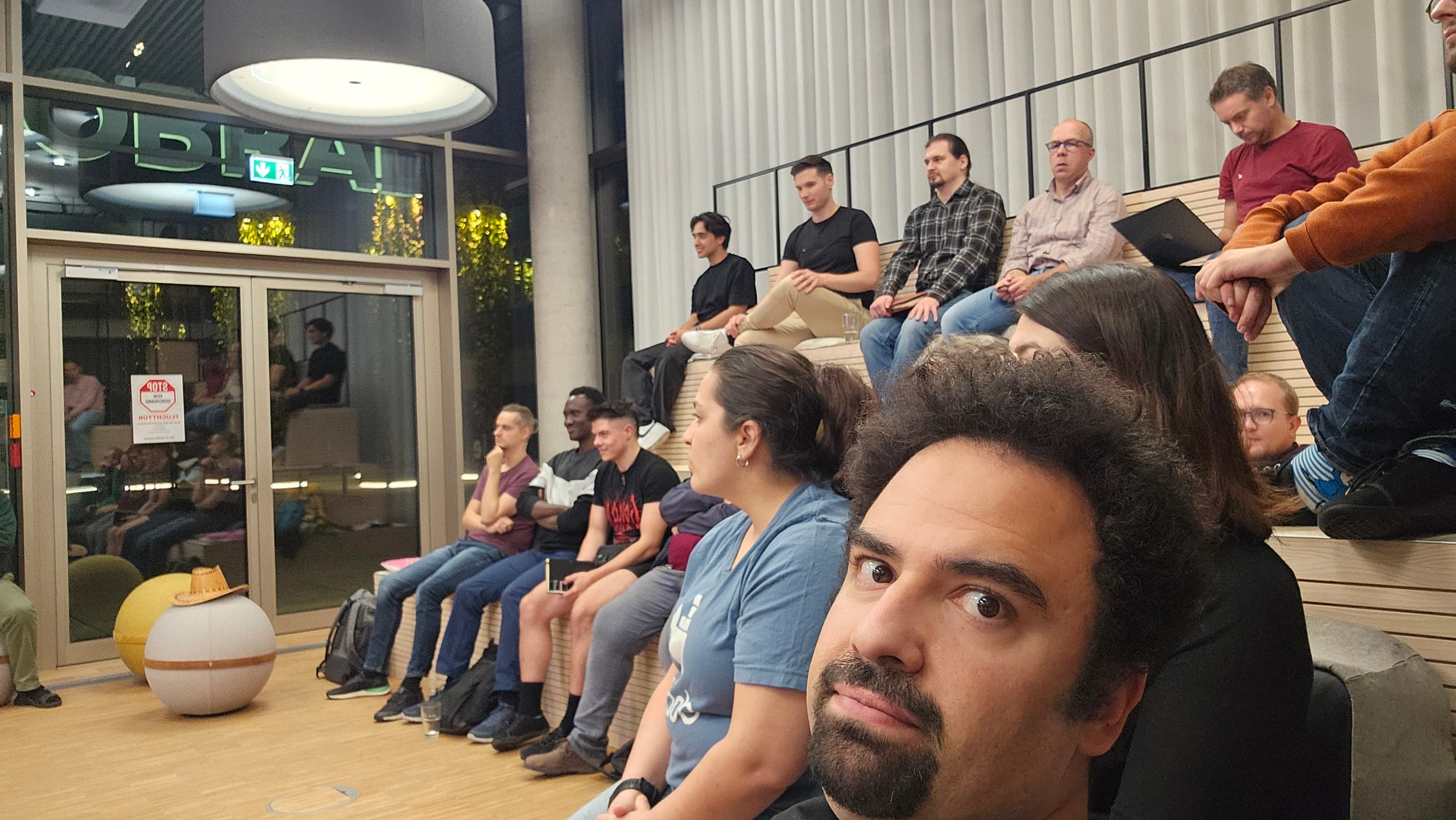 A close-up selfie with rows of attendees watching a talk in the background.