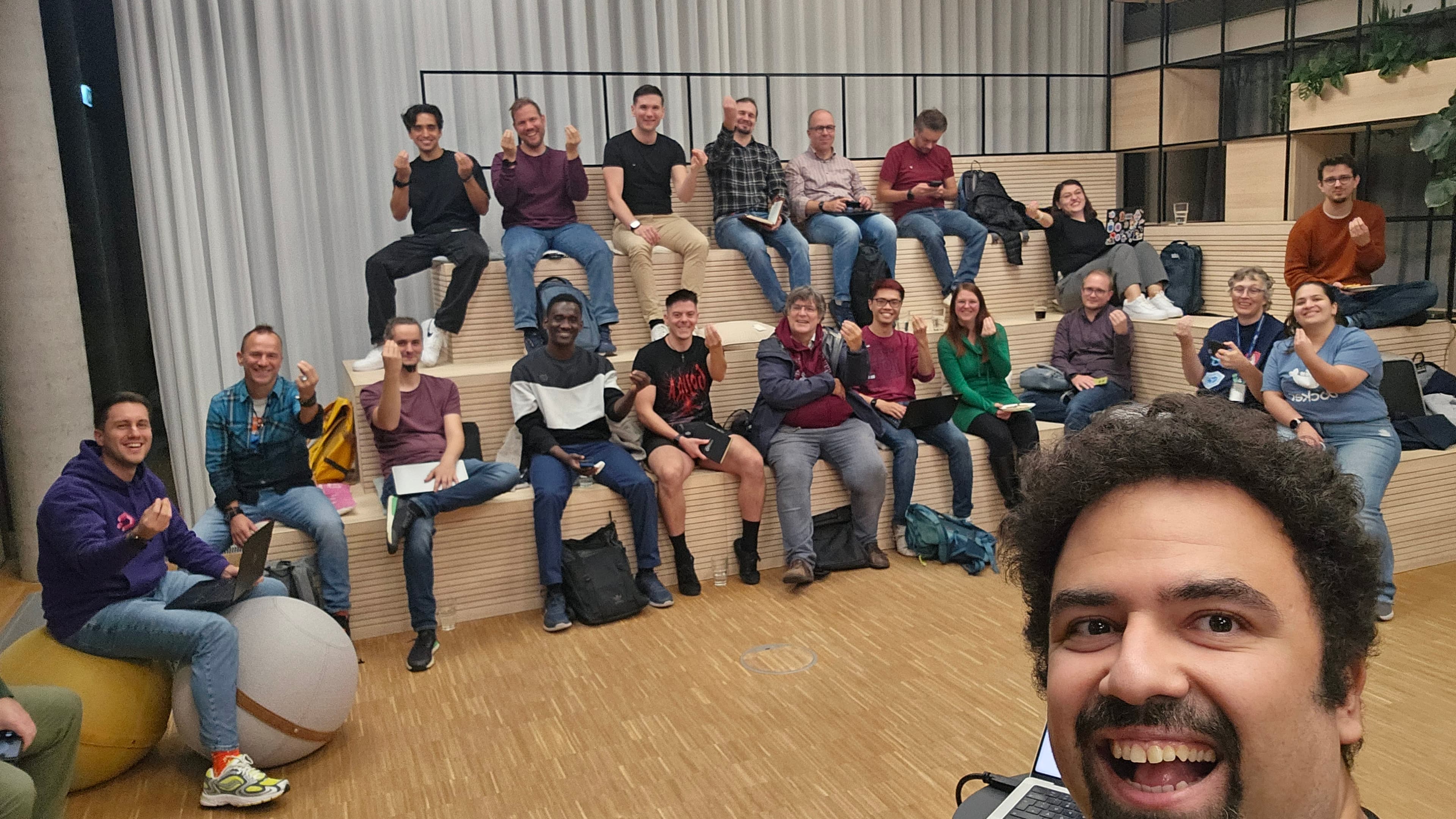 A group selfie with smiling attendees seated on wooden tiers at JobRad.