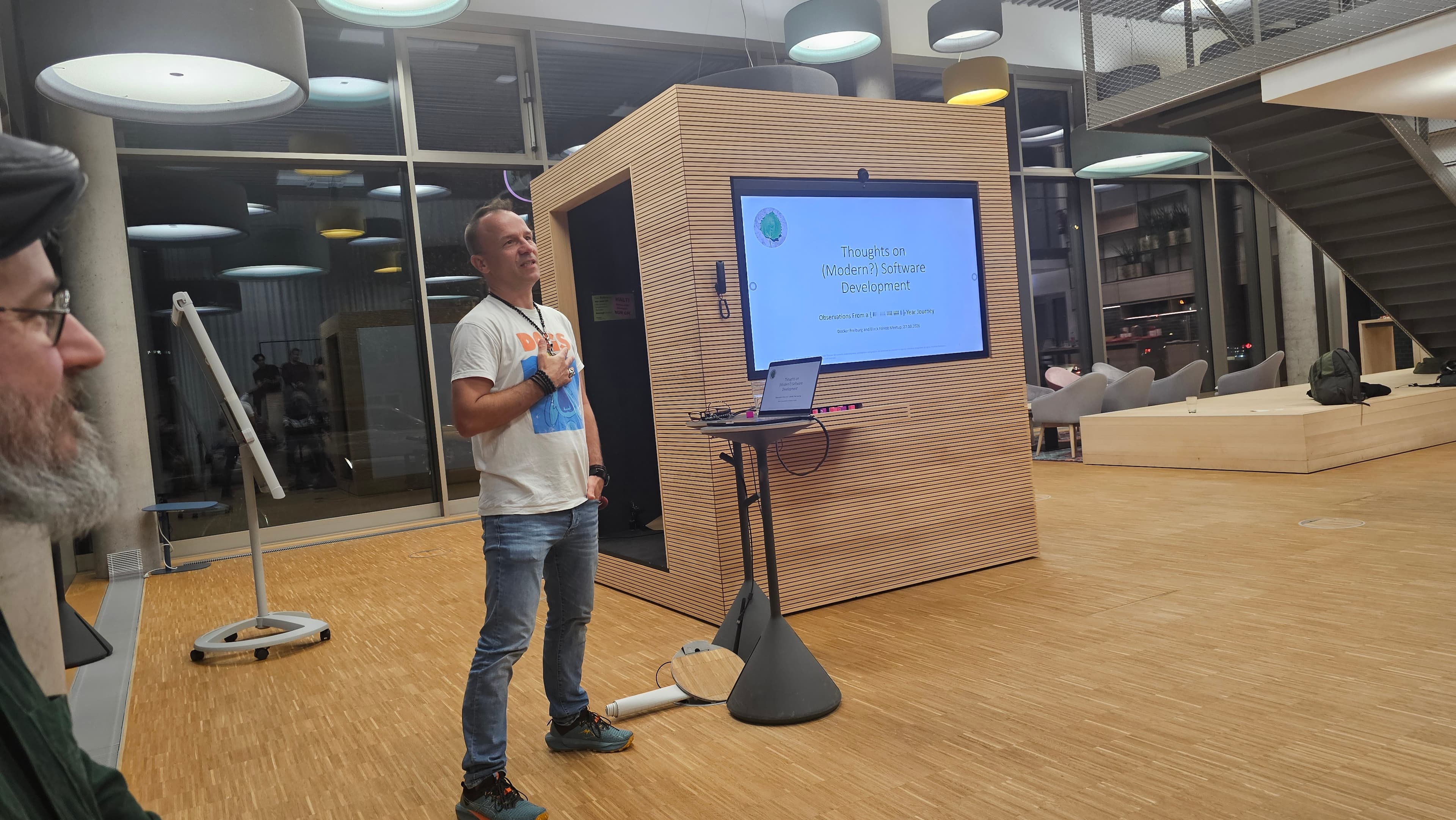 A presenter stands beside the title slide for Thoughts on (Modern?) Software Development.